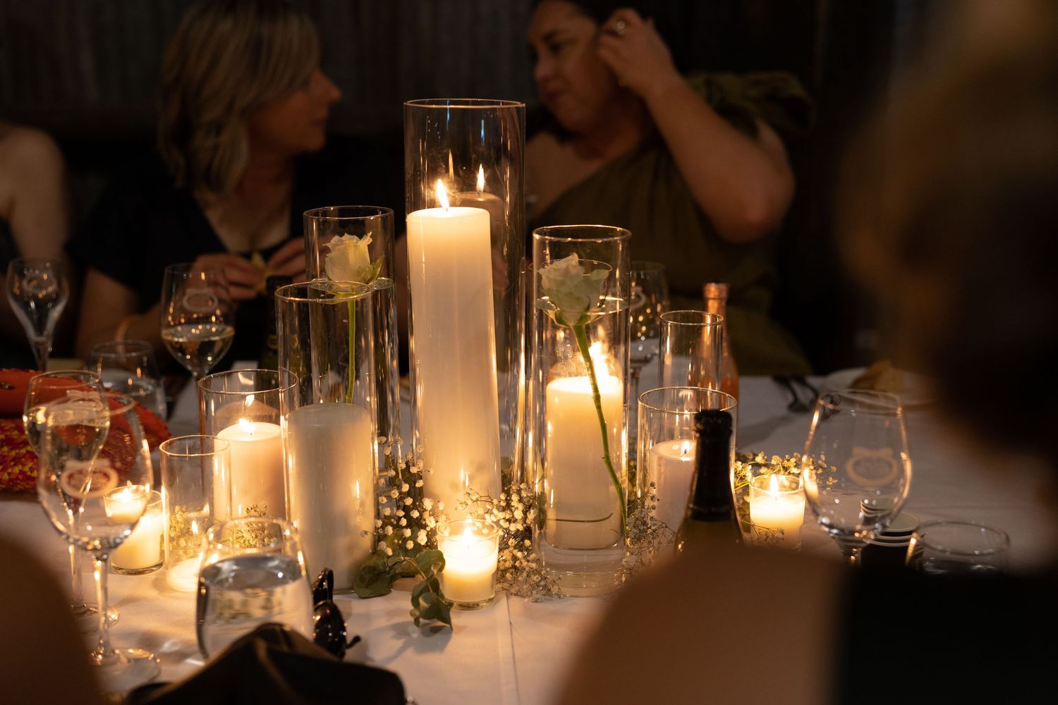Elegant dining table set with glowing candles in glass cylinders creating romantic mood lighting at evening event.