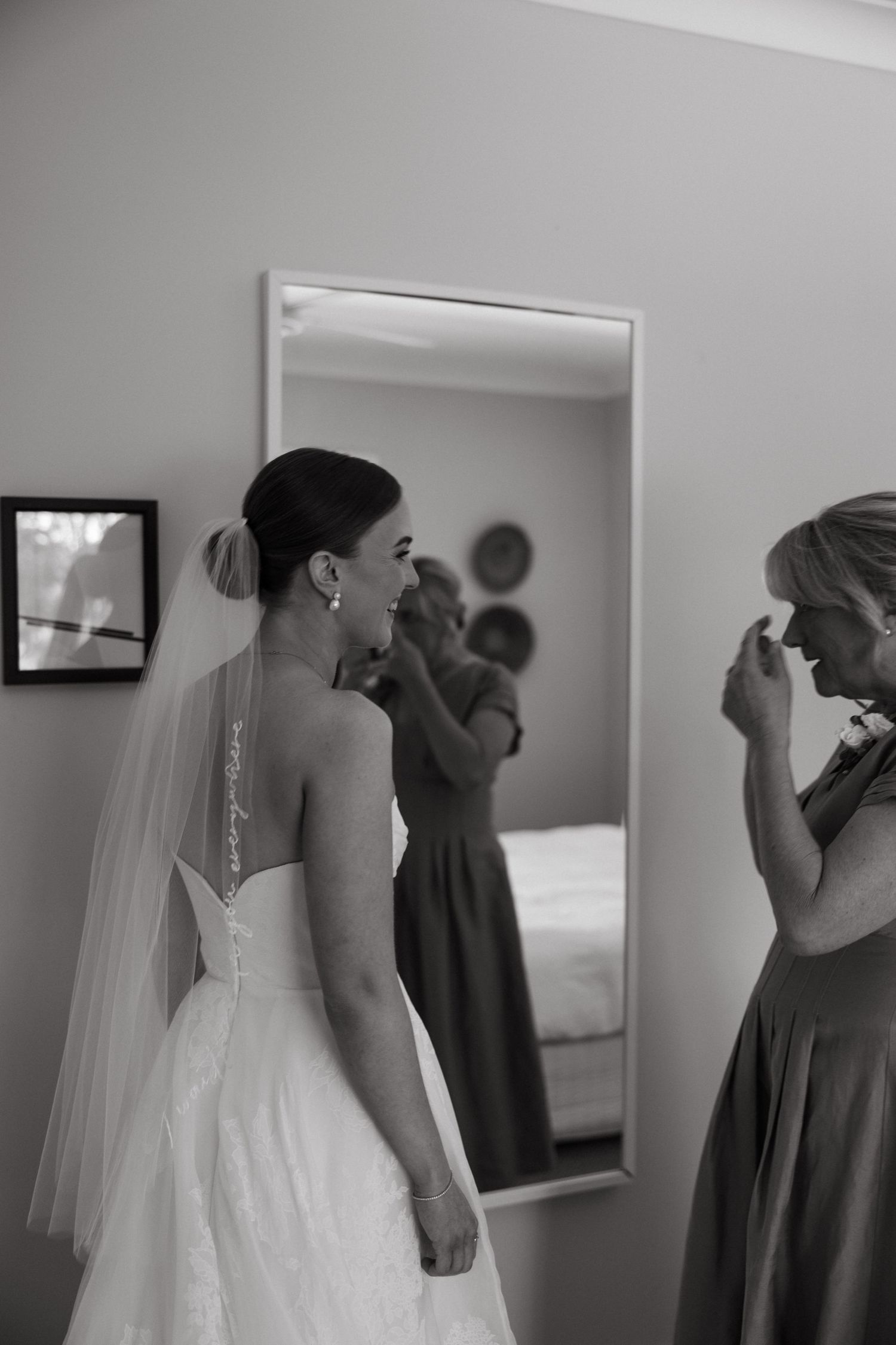 An elegant bride in a strapless wedding dress stands in front of a mirror while getting ready.