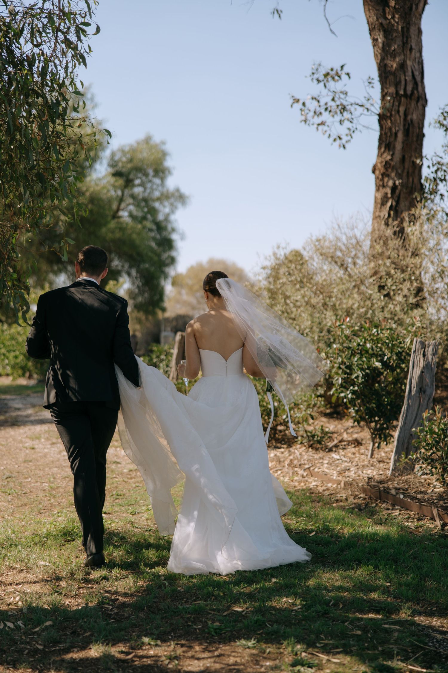 Newlyweds walking hand in hand through a sunny garden path.