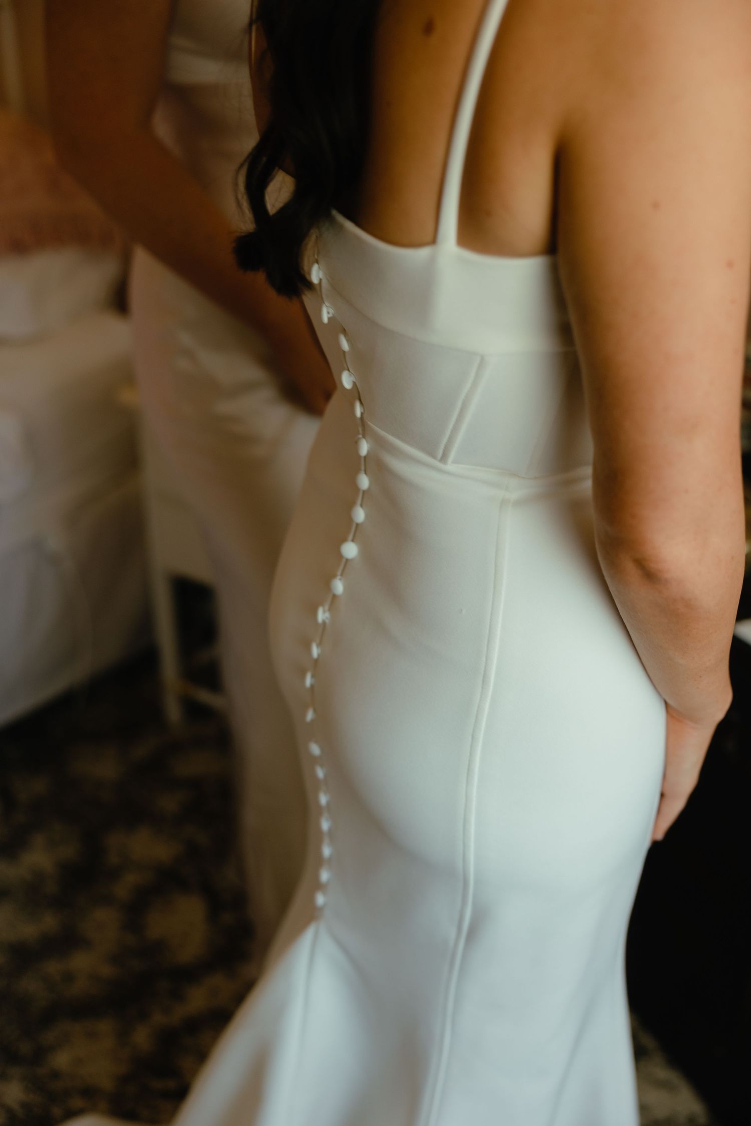Close-up of a white wedding dress showing delicate button details along the back.