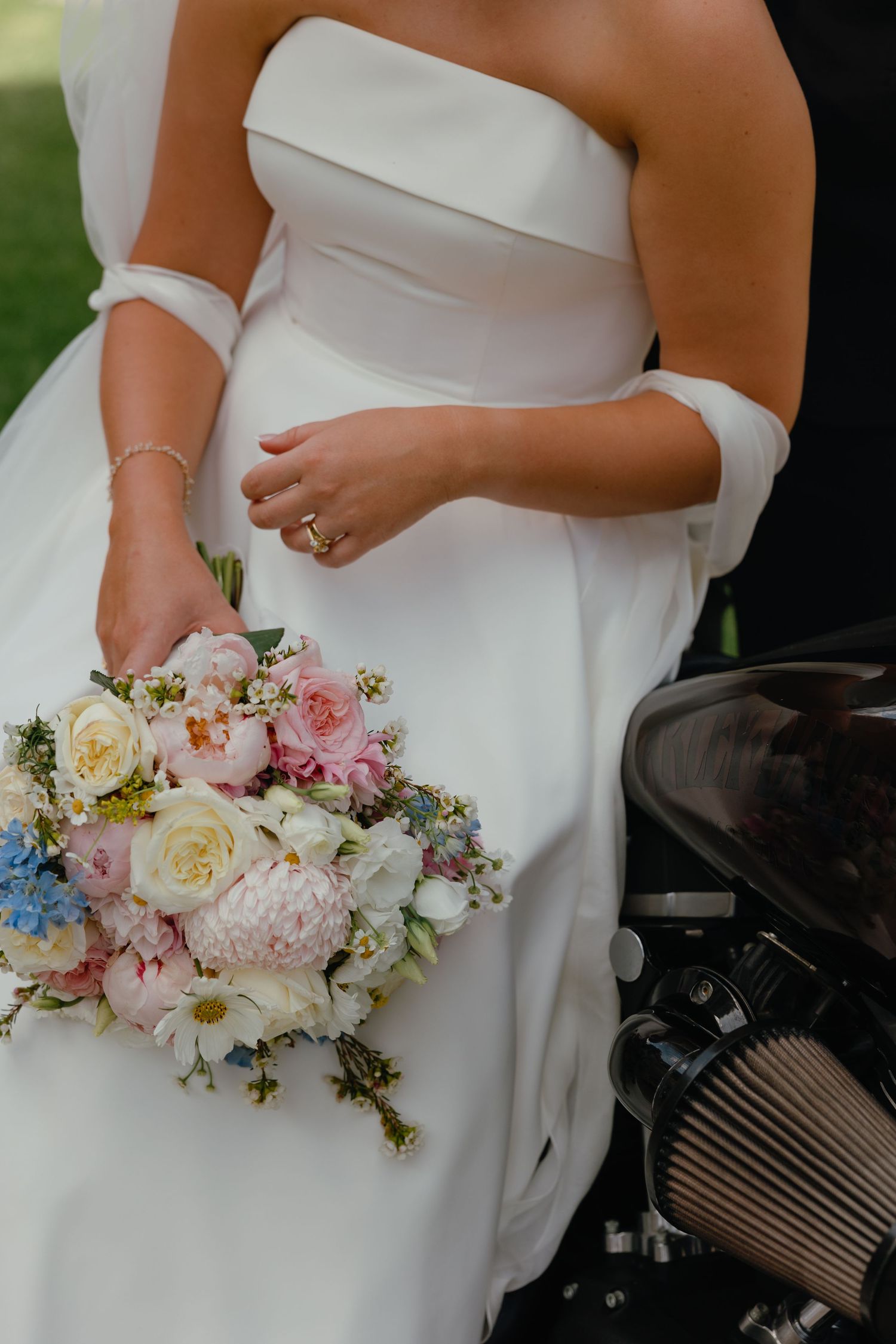 Close-up of wedding dress detail and delicate pink and white floral bouquet against ivory fabric.