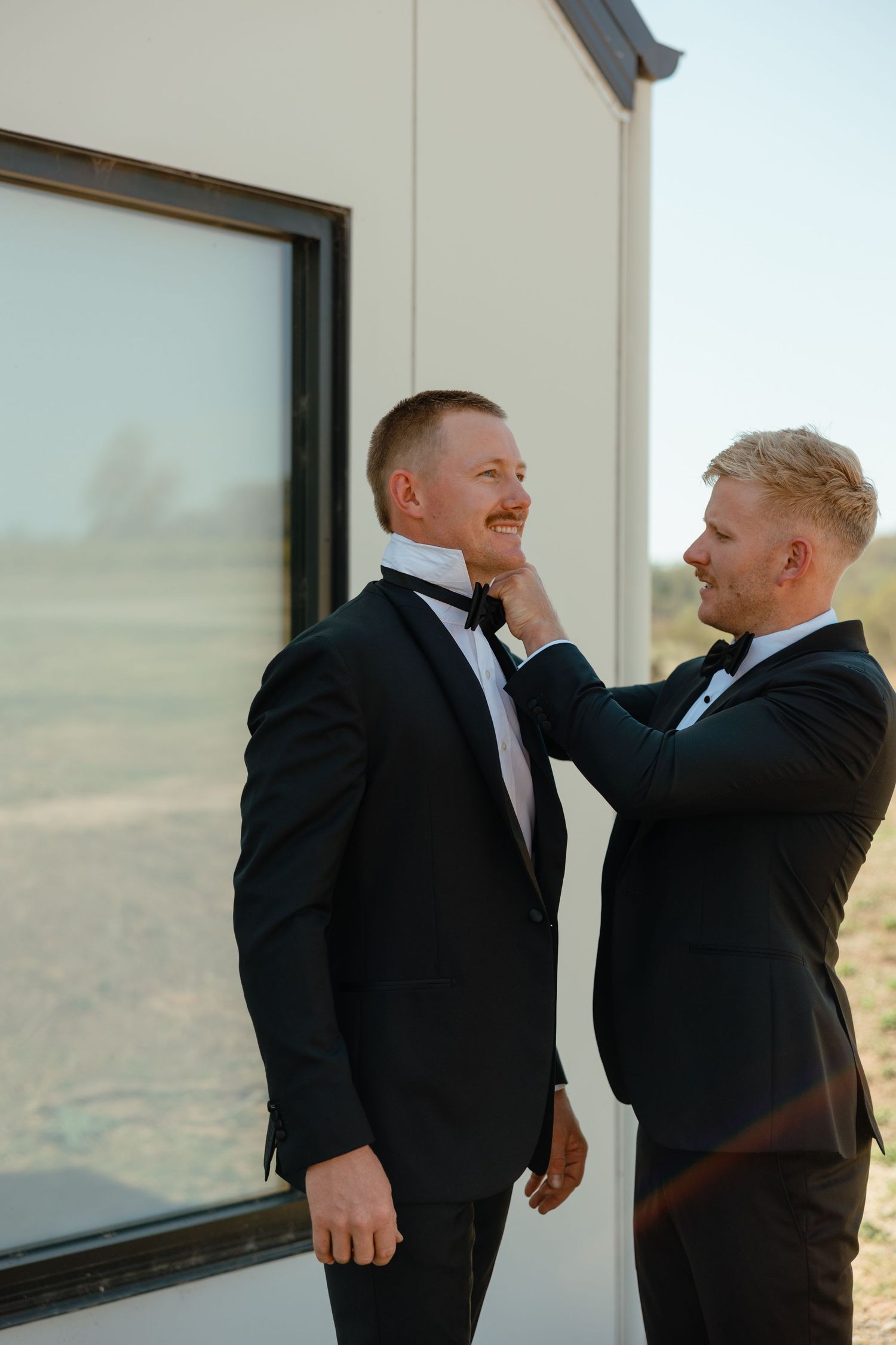 Two people in tuxedos sharing an intimate moment during a wedding photoshoot.
