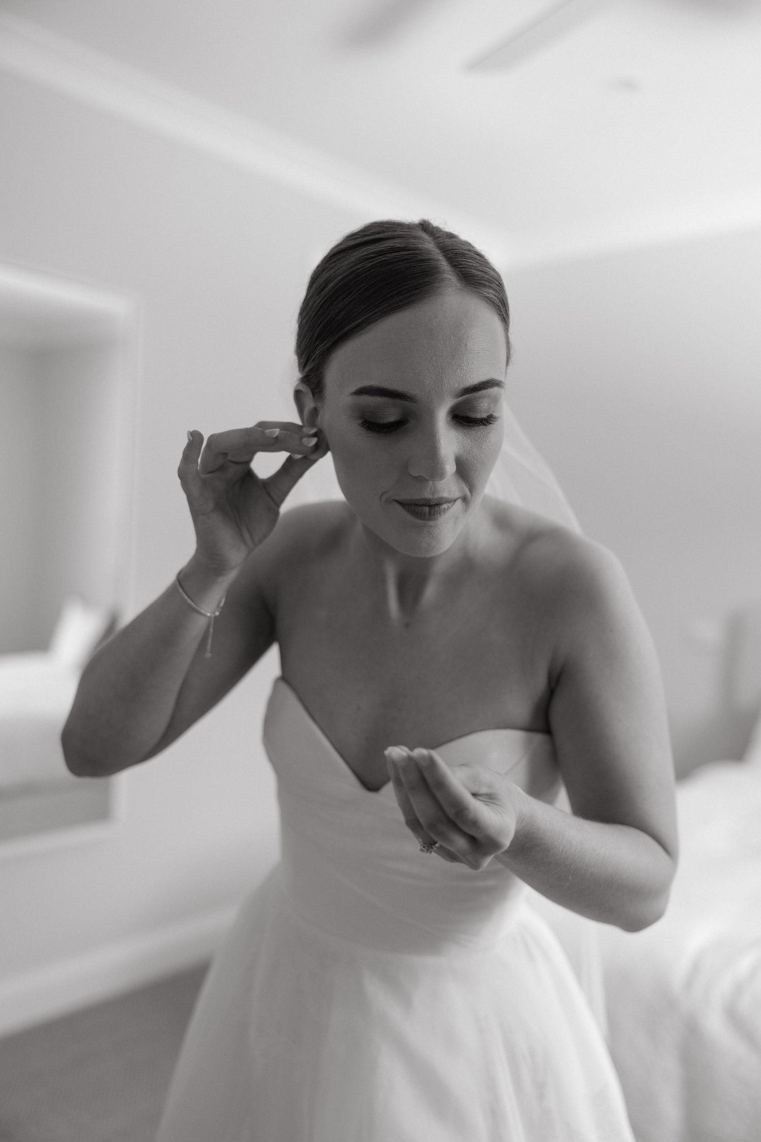 A bride in a strapless white gown puts on her finishing touches while getting ready for her wedding day.