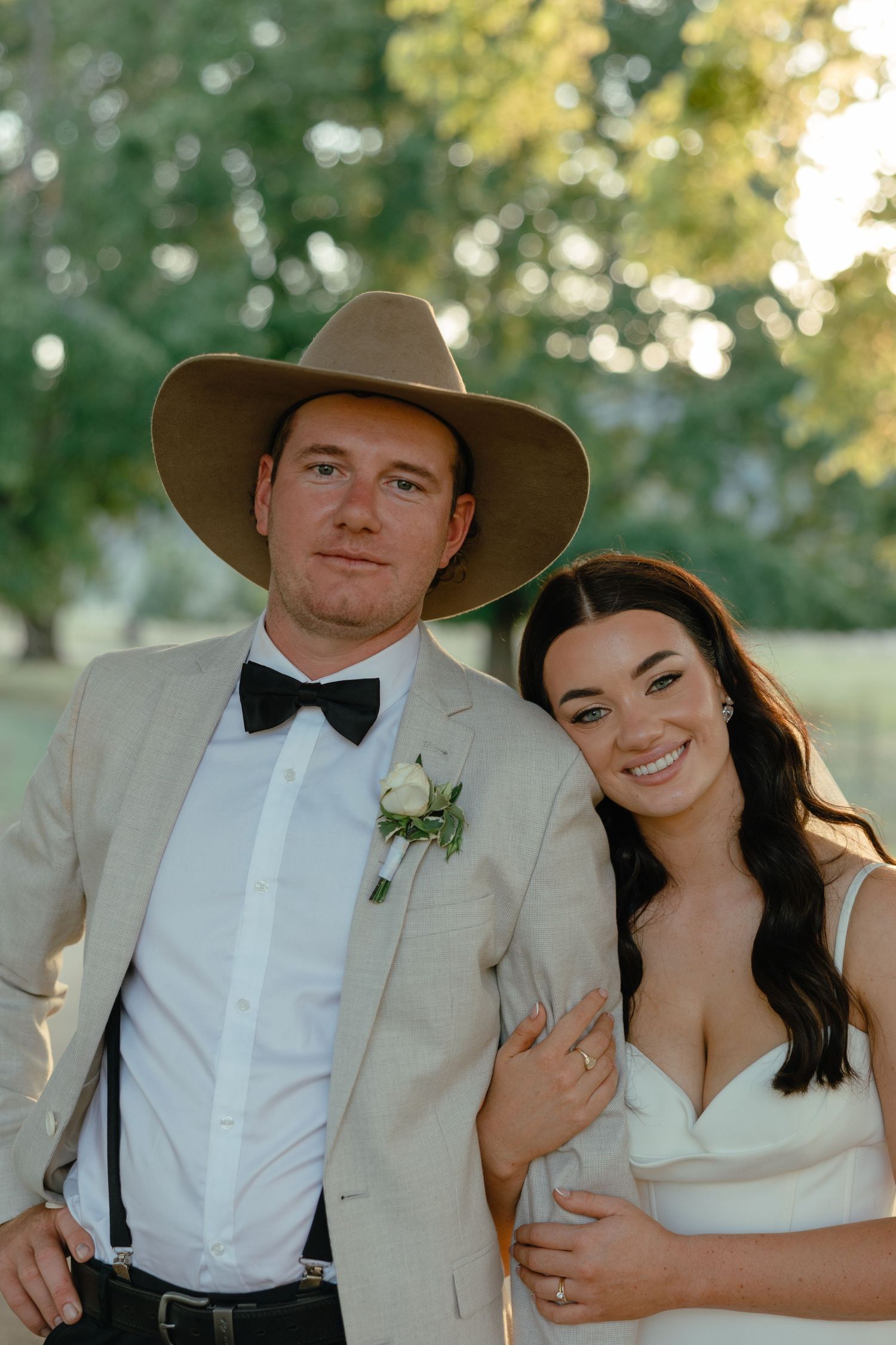 A couple celebrates their wedding day in western-inspired attire with a cowboy hat and formal dress.