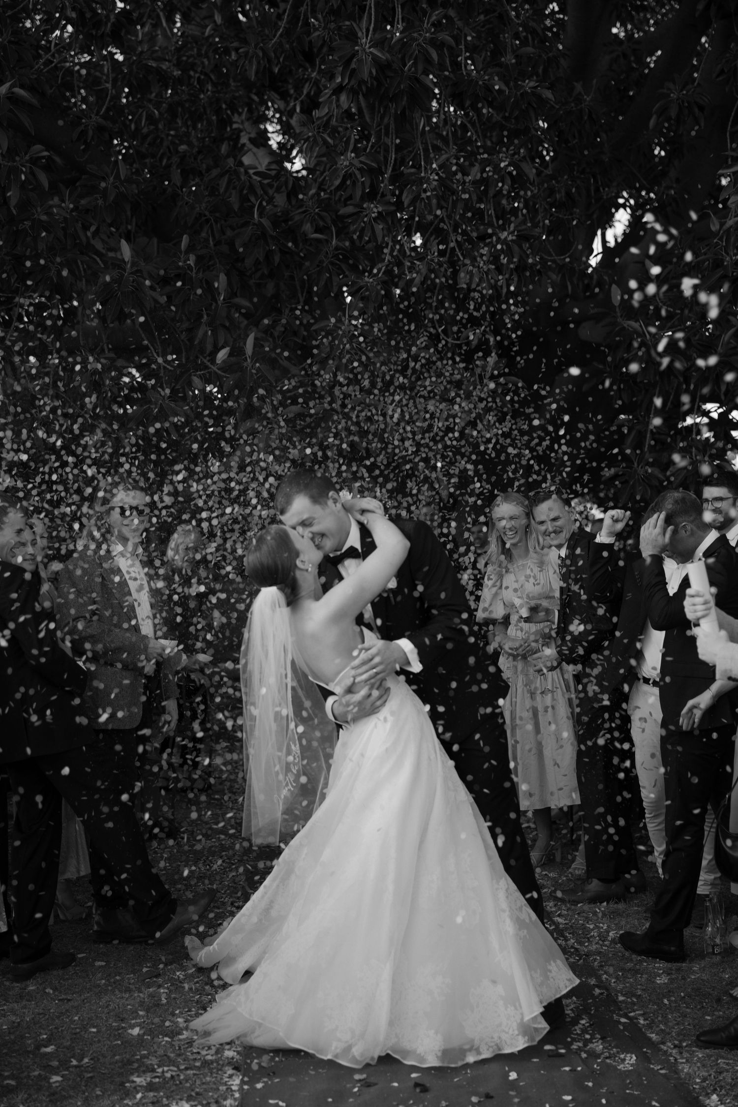 Couple sharing their first dance surrounded by falling confetti in black and white.