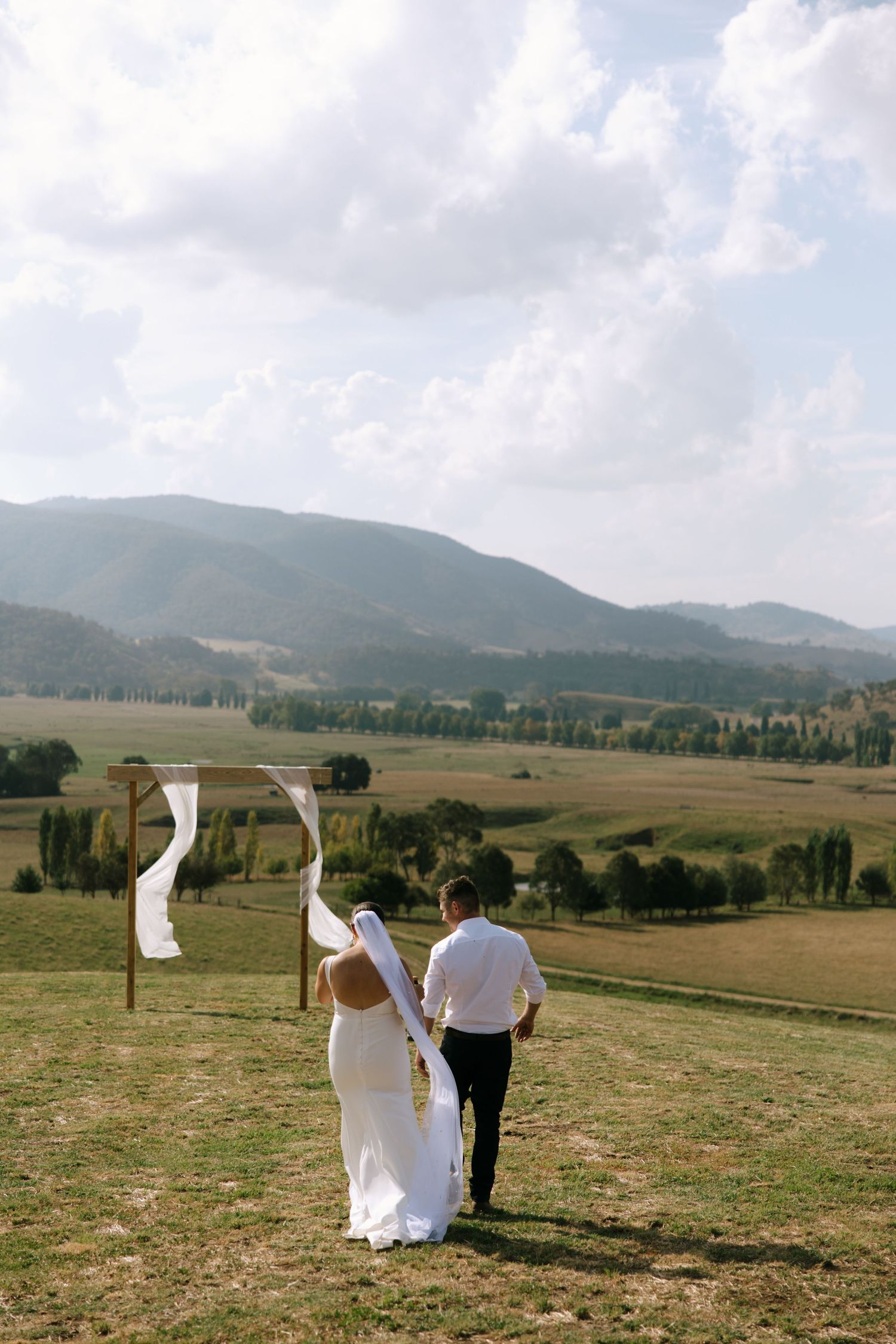 Couple walking away from wooden arch towards mountain vista.