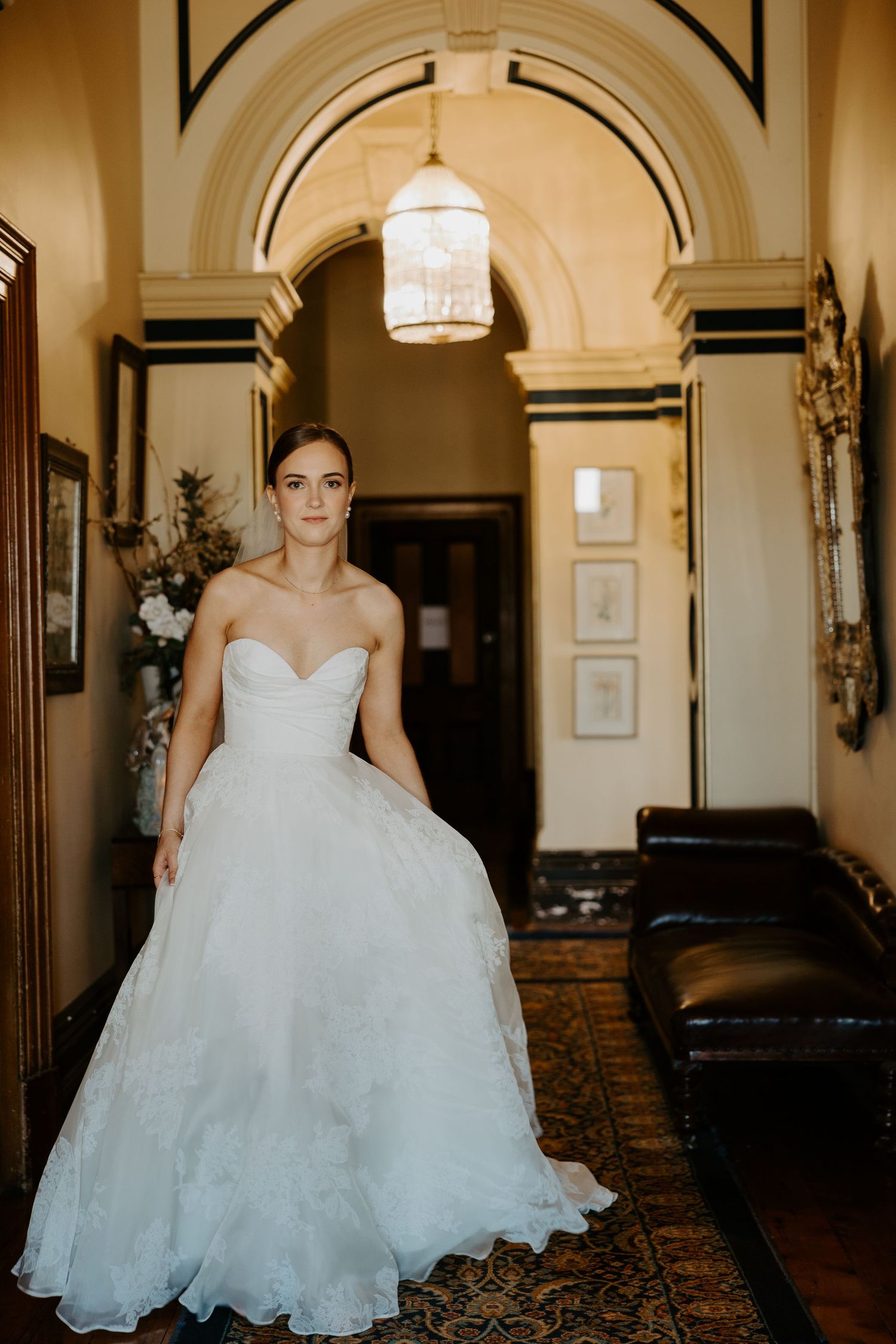 A bride in a sweetheart neckline ballgown poses beneath an ornate archway with warm lighting.