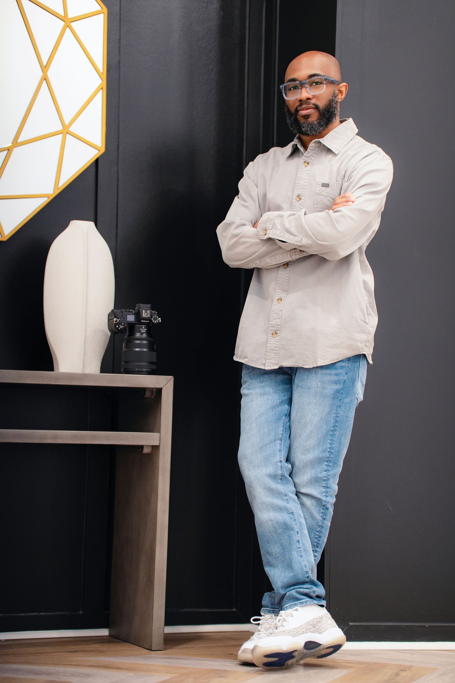 Professional photographer in casual attire standing beside equipment in modern studio setting.