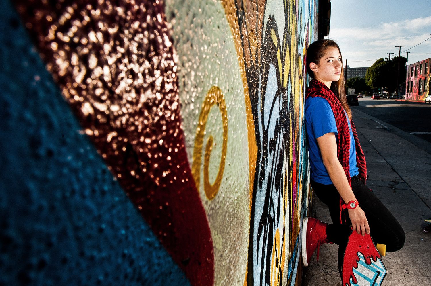 Urban street scene against a graffiti wall with a person in red outfit holding sports equipment in a dramatic pose.