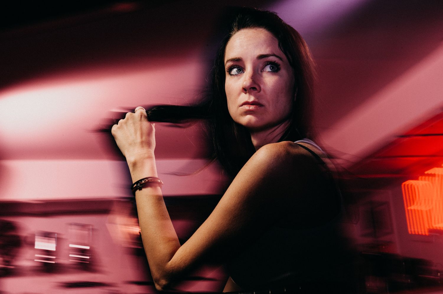 Dramatic portrait in red lighting showing figure holding object with artistic motion blur effect.
