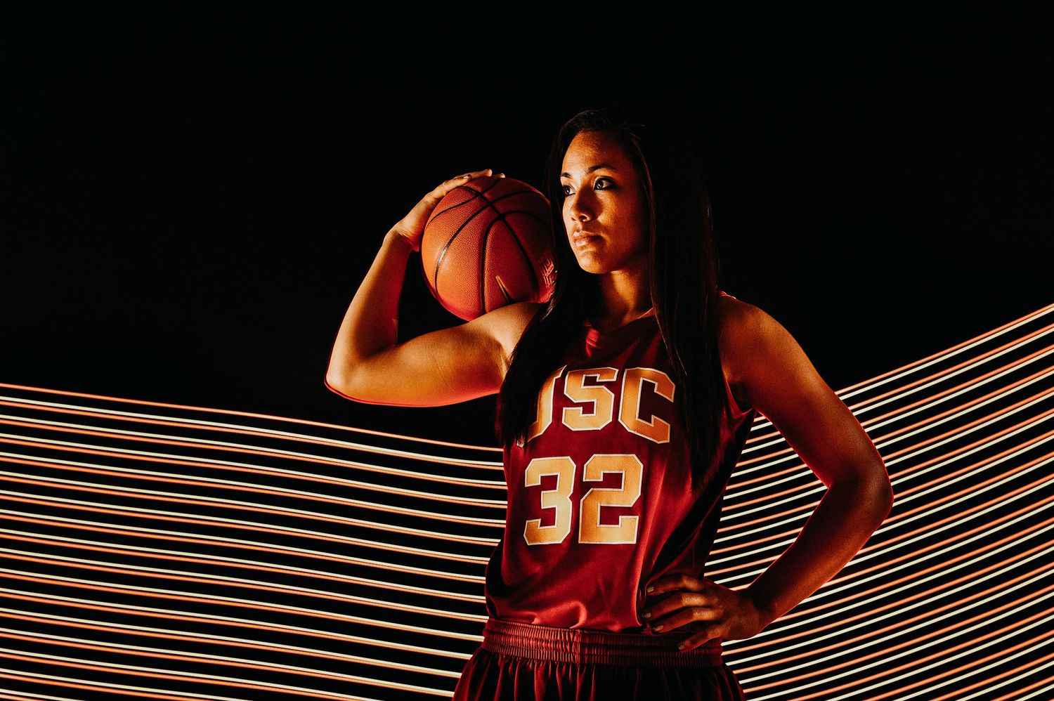 Basketball player wearing USC jersey number 32 poses with ball against dark background with striped lighting effect.