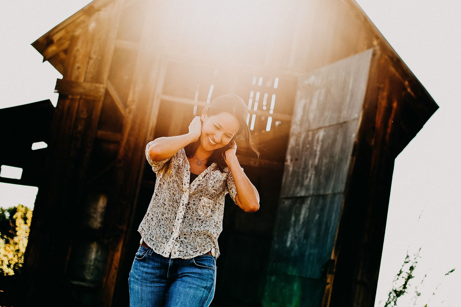 Candid outdoor photograph of person in spotted blouse and jeans with sunlit building in background.