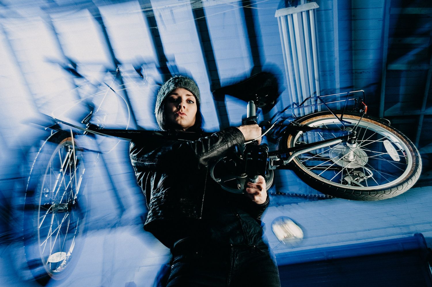 Action shot captured in a blue-lit setting shows someone lifting a BMX bicycle overhead in a dramatic pose.