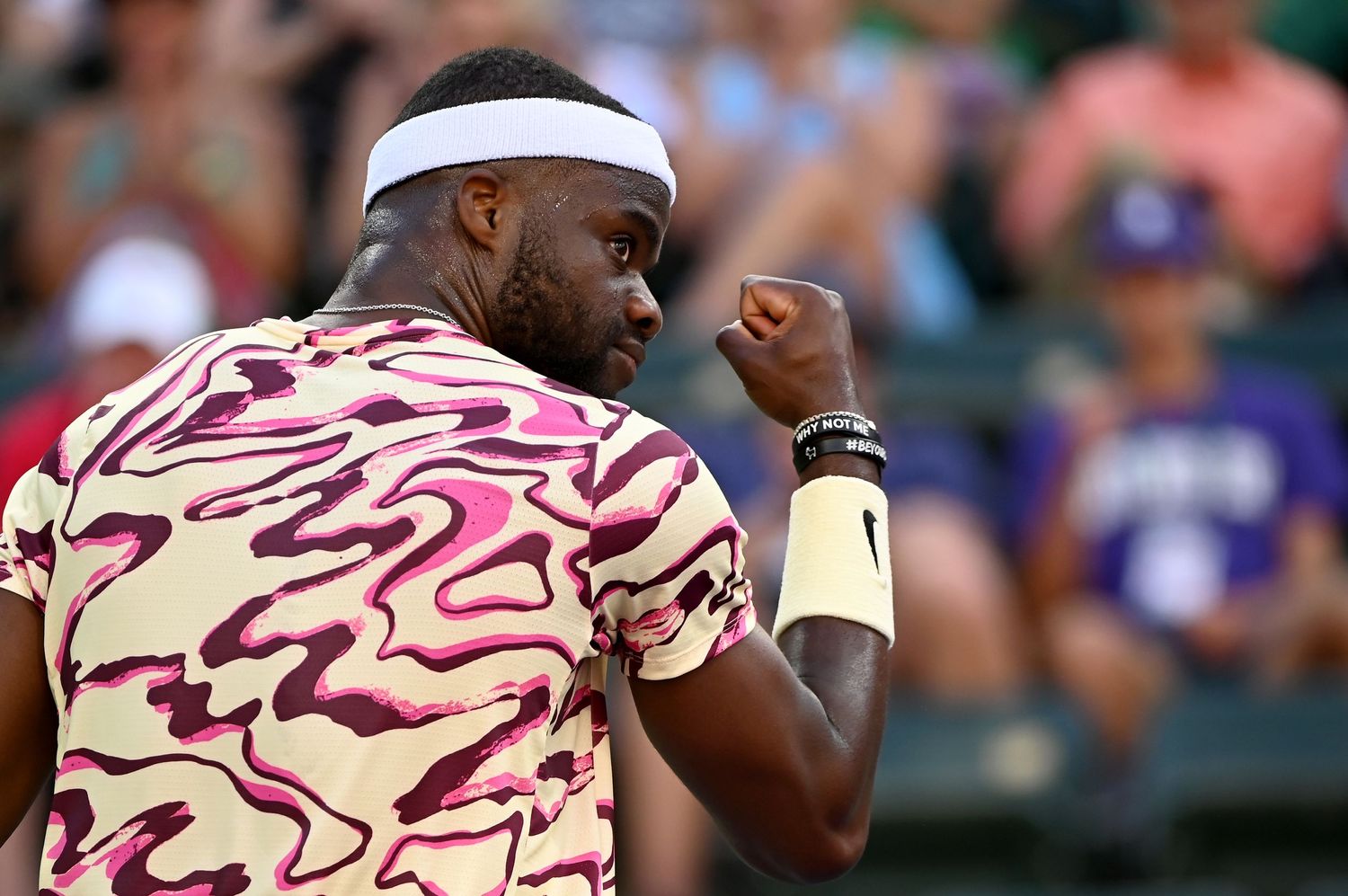 Tennis player wearing a white headband and cream-colored shirt with pink pattern celebrates during a match.