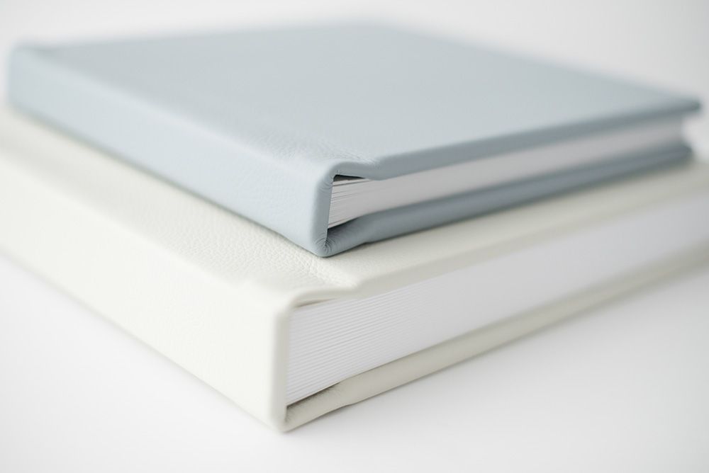 Minimalist photo albums in light blue and white stacked together against white background.