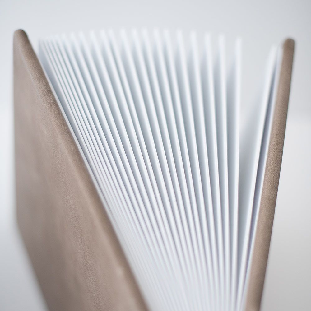 Macro shot of crisp white pages fanned out between beige album covers.