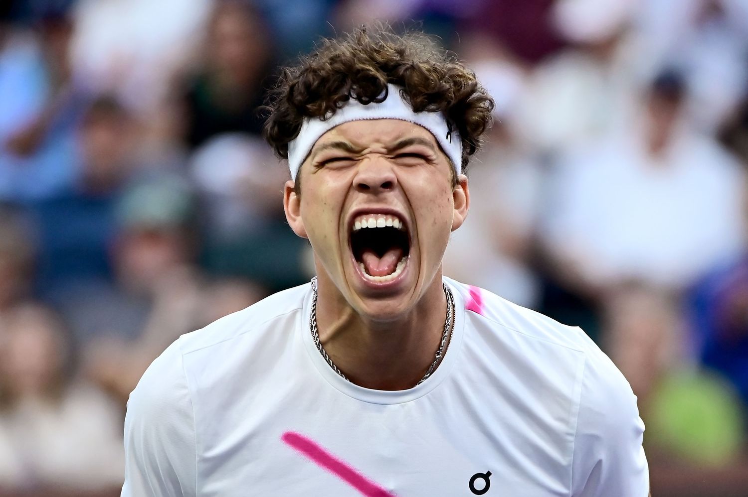 A tennis player in a white outfit with headband celebrates with intense emotion during a match.