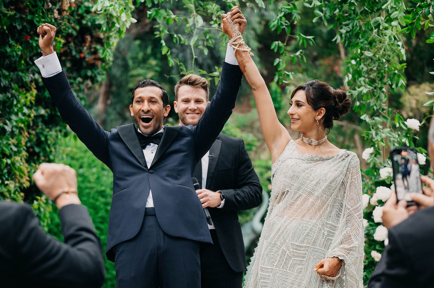 A joyous celebration moment under leafy green vines at an outdoor wedding ceremony.
