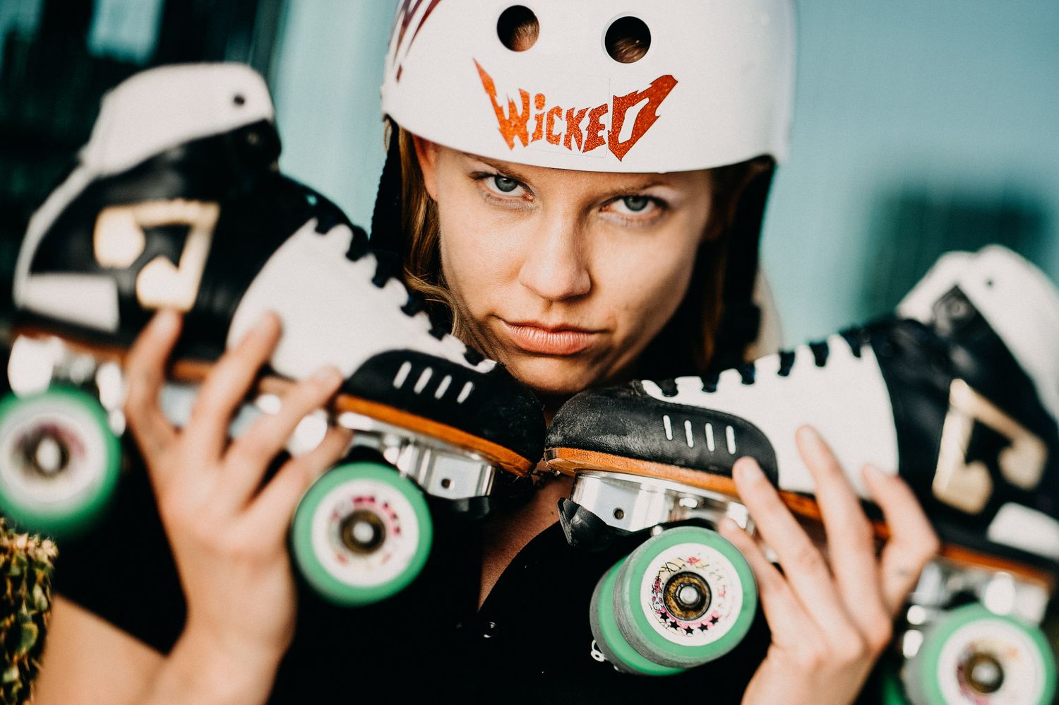 Skater in white helmet holds roller skates with mint green wheels against blue-tinted background.
