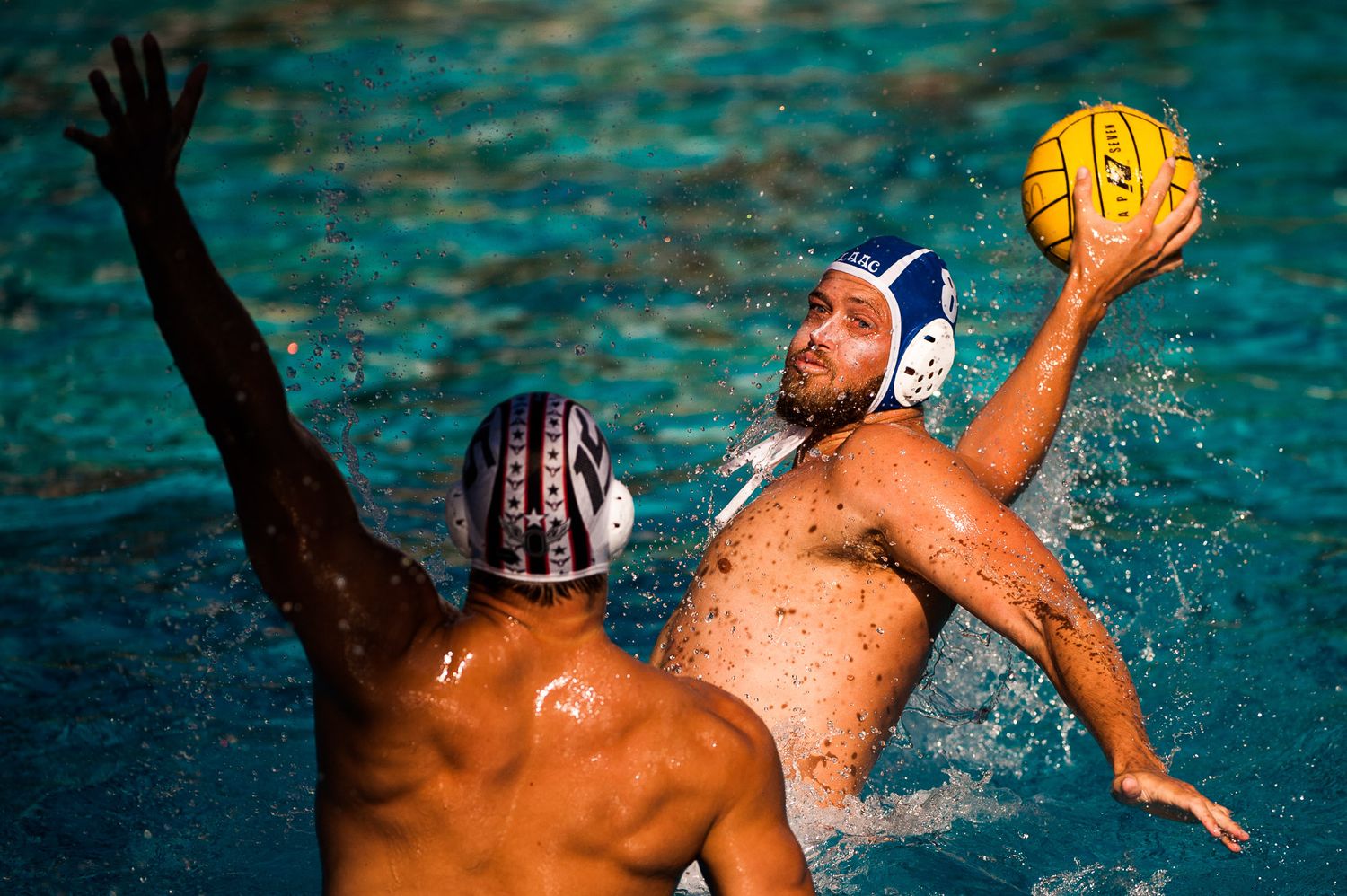 Two water polo players compete for the yellow ball during an intense match in turquoise blue water.