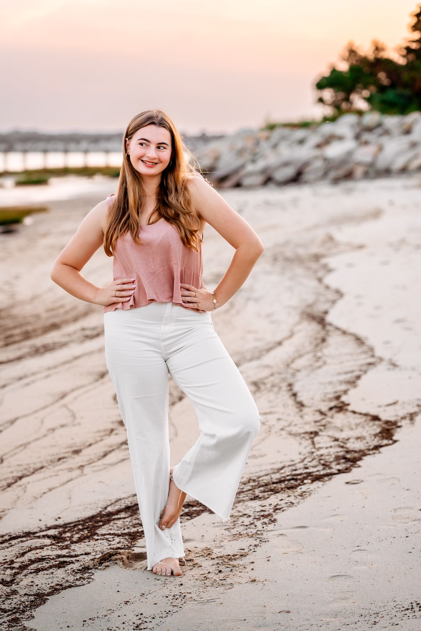 Woman in casual attire posing on beach at sunset.