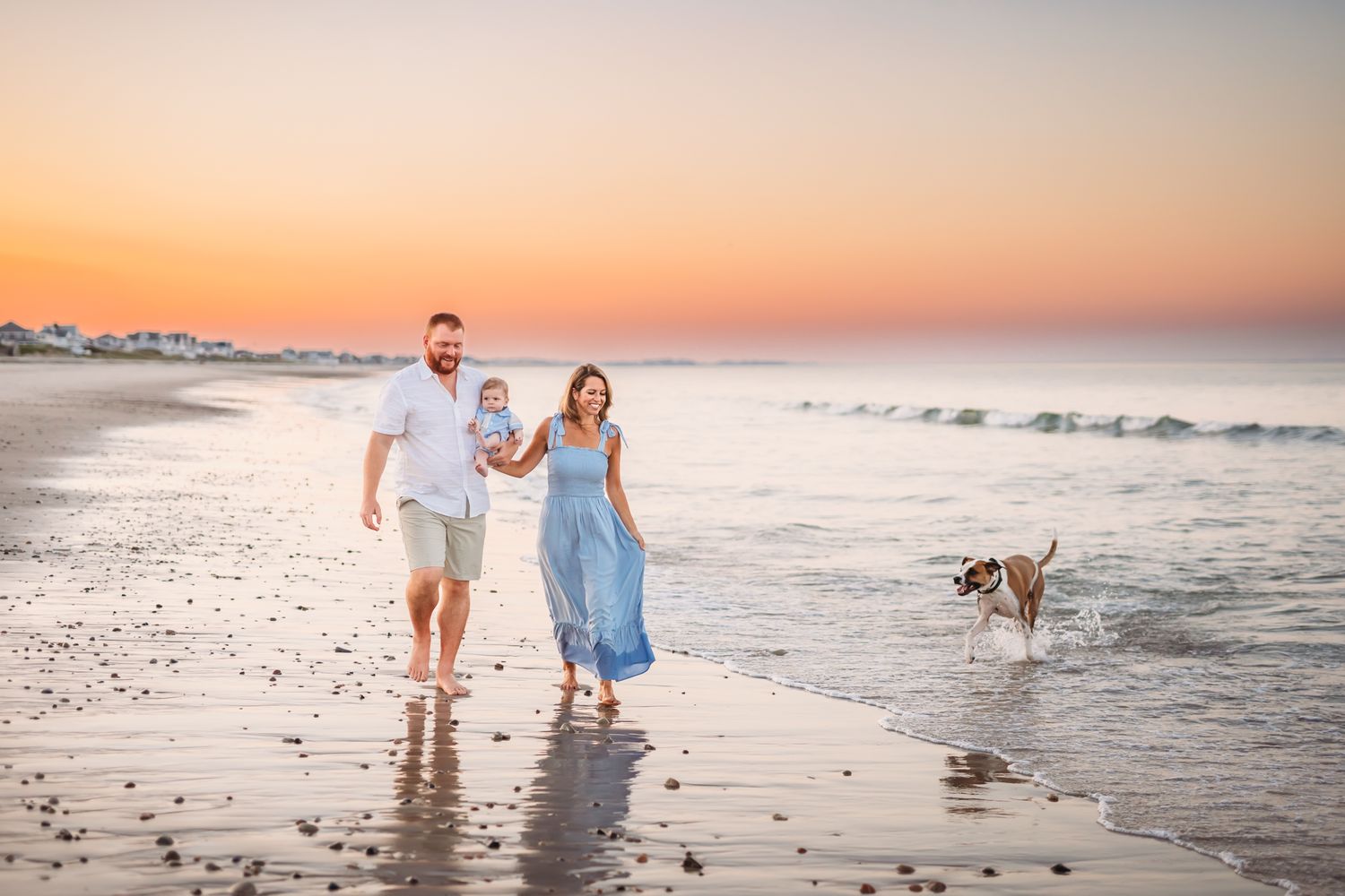 A couple and their dog walking along the beach shore during a beautiful sunset.
