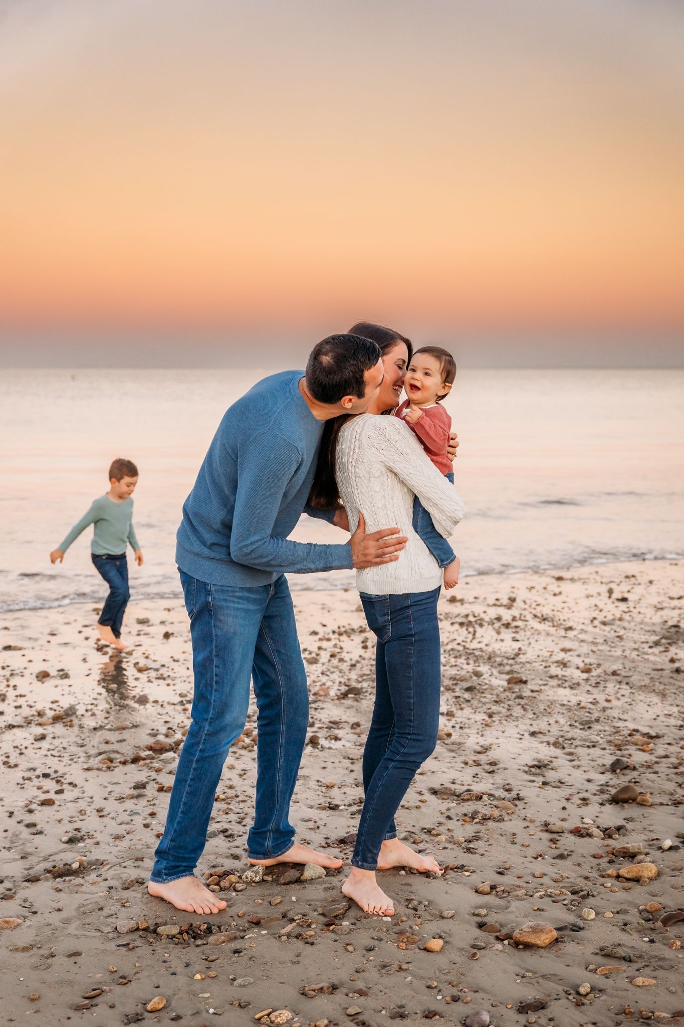 A loving family shares a tender moment together on a beach at sunset while walking barefoot in the sand.