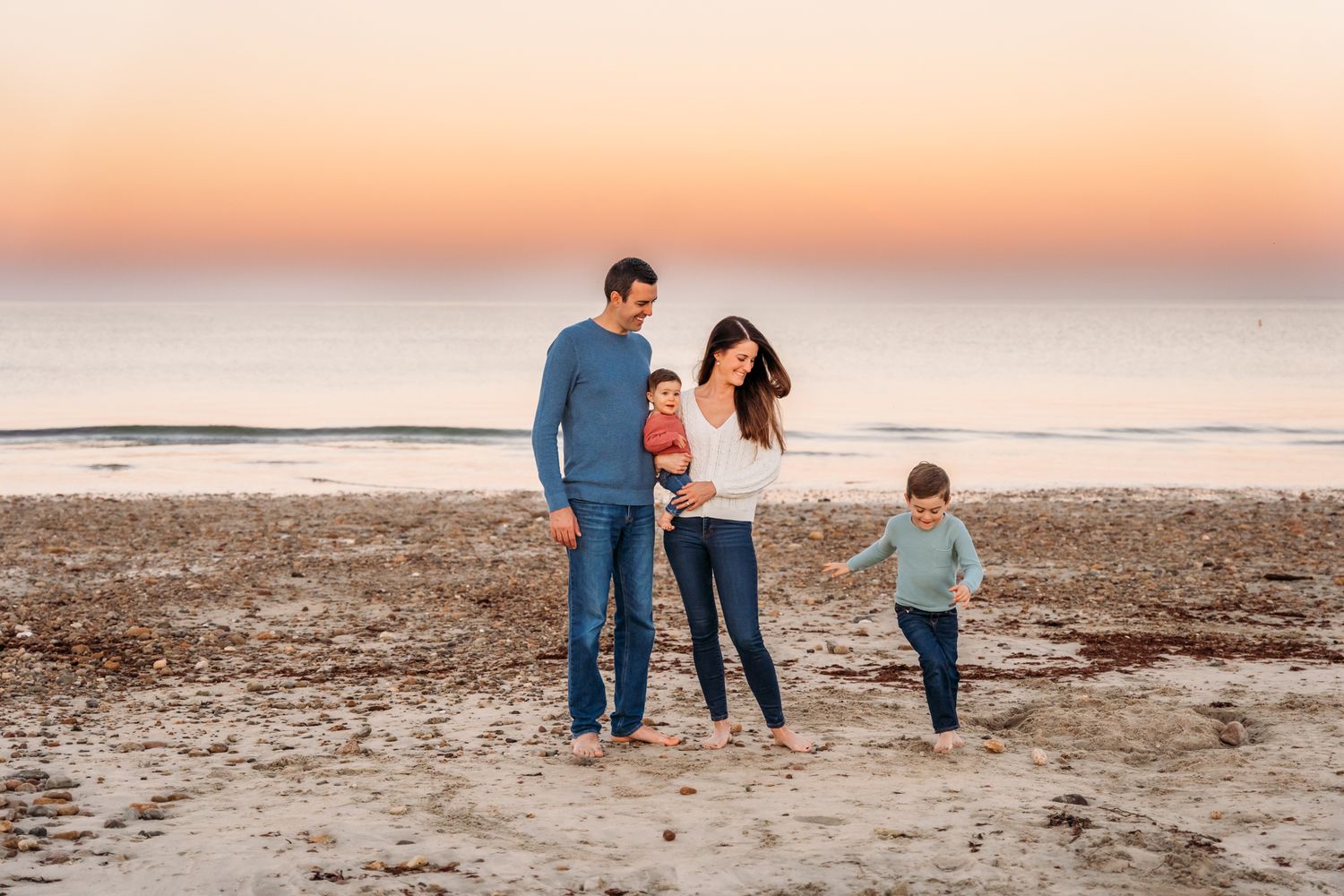 A family walks together on a sandy beach at sunset with warm golden light reflecting off the ocean.