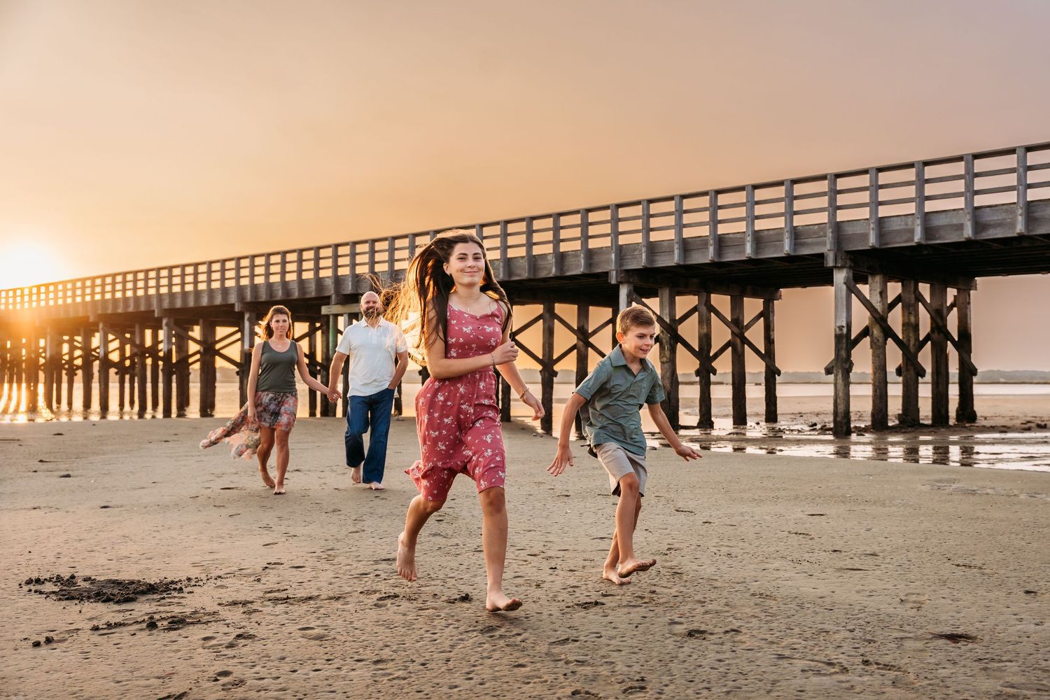 People running and playing near a wooden pier during a golden beach sunset.