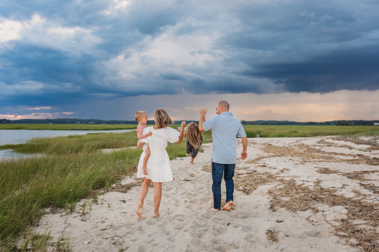 Family walking together on sandy beach path under dramatic stormy sky.
