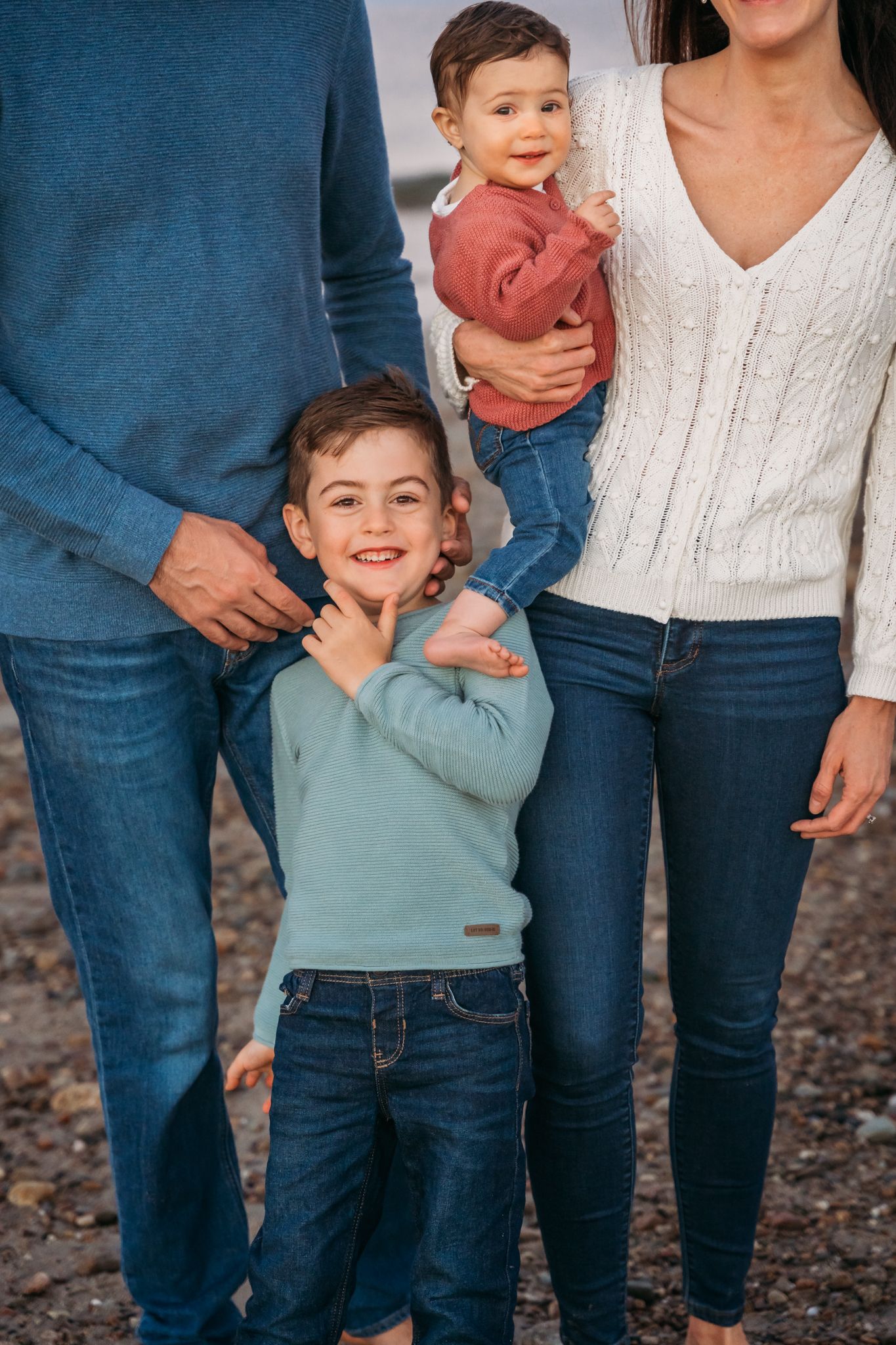 Family of four poses together outdoors wearing blue and white outfits with parents in jeans and children in casual attire.