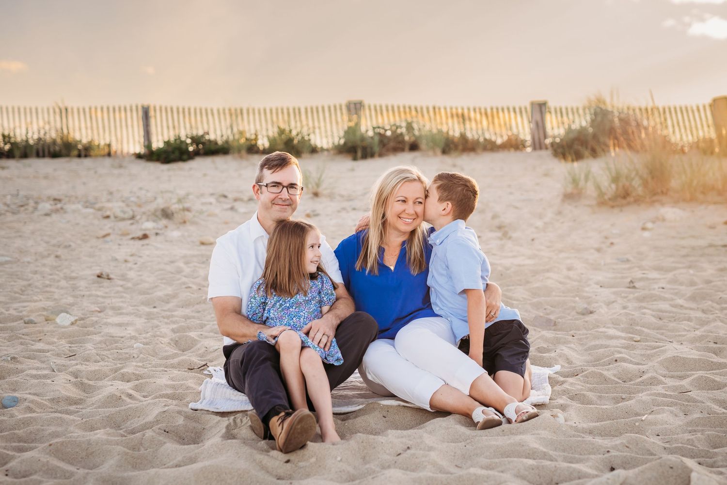 Family spends quality time together sitting on a sandy beach during golden hour at sunset.