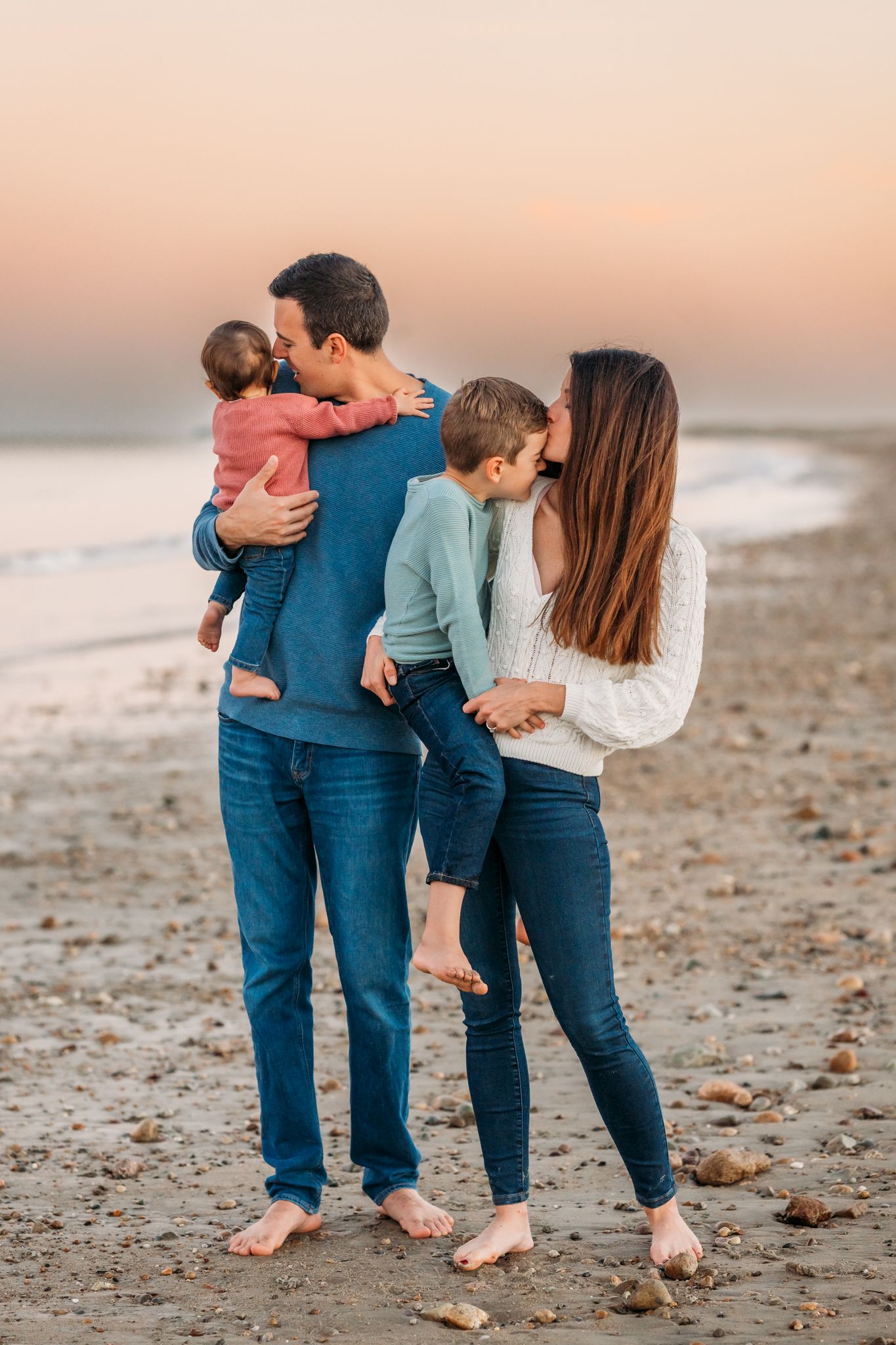 Family sharing a tender moment together on the beach at sunset with bare feet in the sand.
