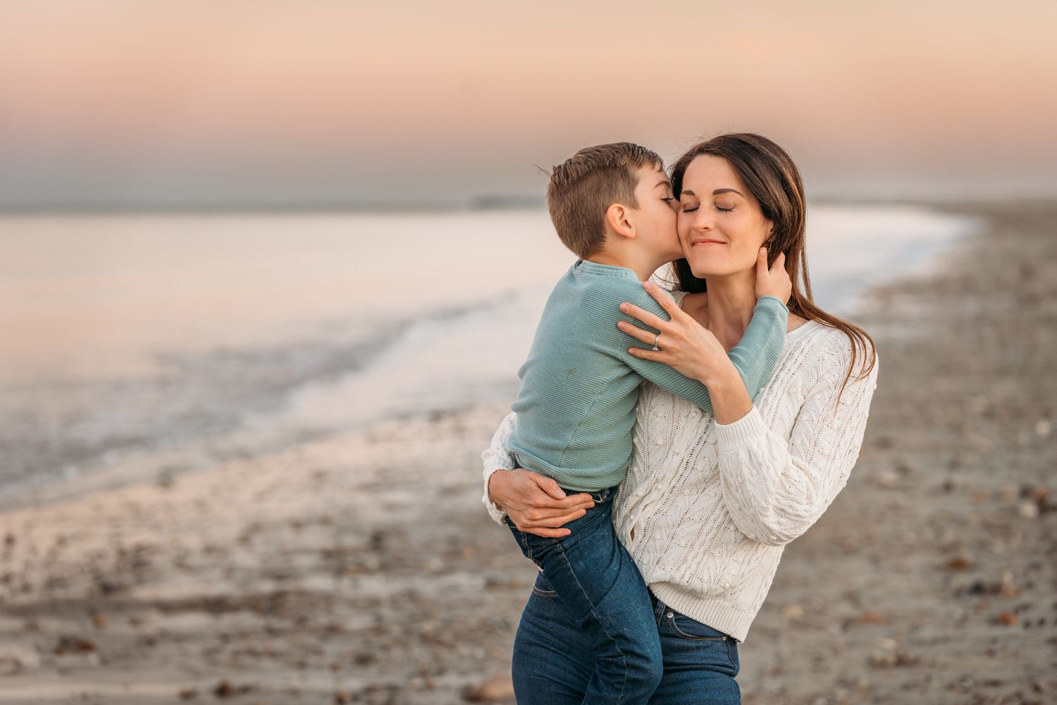 A tender moment between parent and child embracing on a sandy beach during sunset.