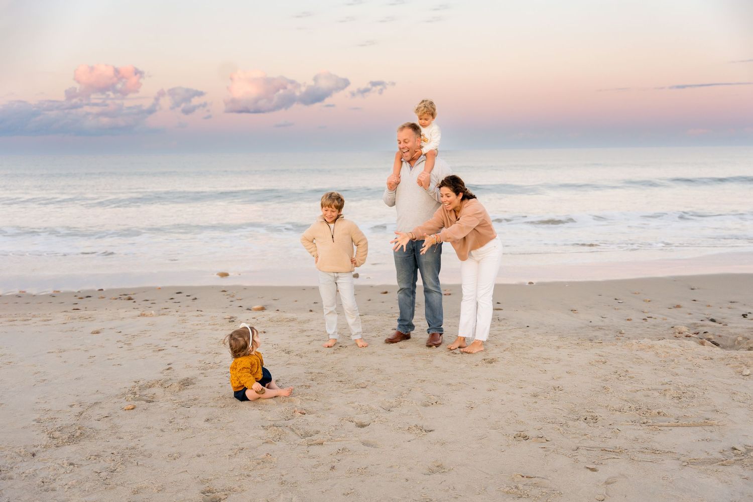 Group gathered on beach at sunset with dramatic pink sky and ocean waves.