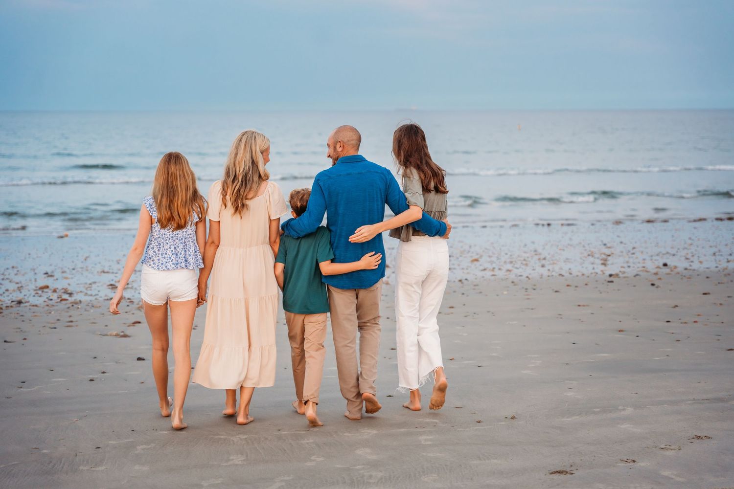 A group walking together on a beach at sunset, their backs to the camera as they face the ocean view.
