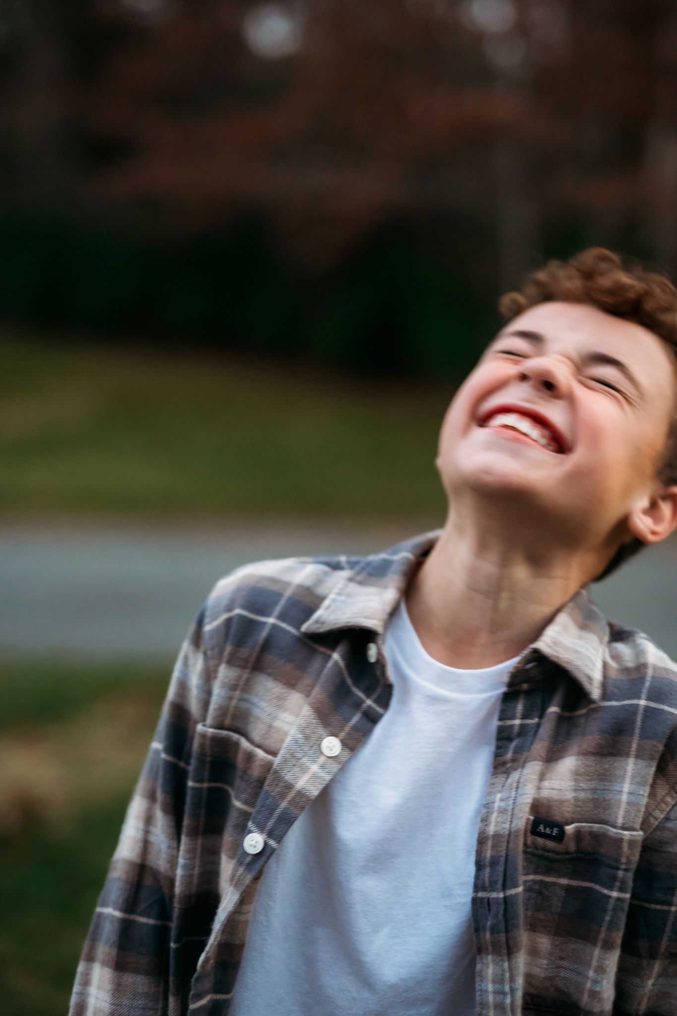 Youth laughing joyfully while wearing plaid flannel shirt outdoors.