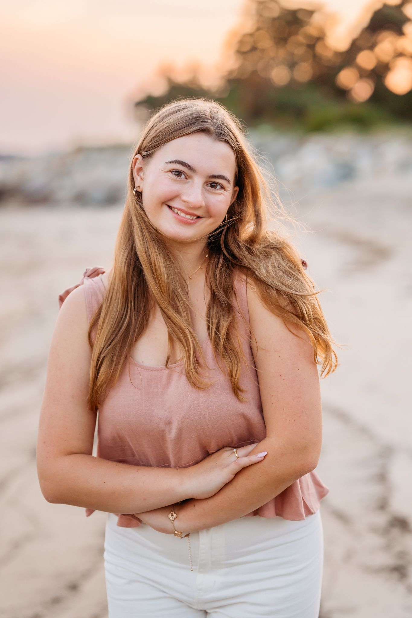 Sunset portrait on beach wearing pink top and white pants with golden bokeh lighting in background.