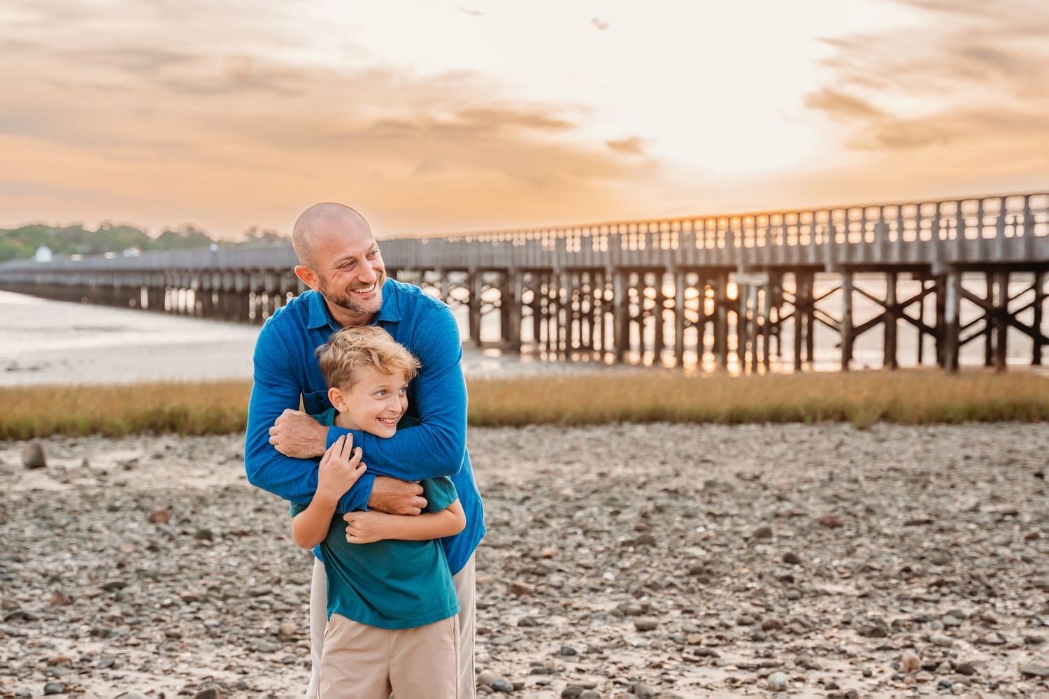 A warm sunset over a wooden pier as two people share a tender moment on the beach.
