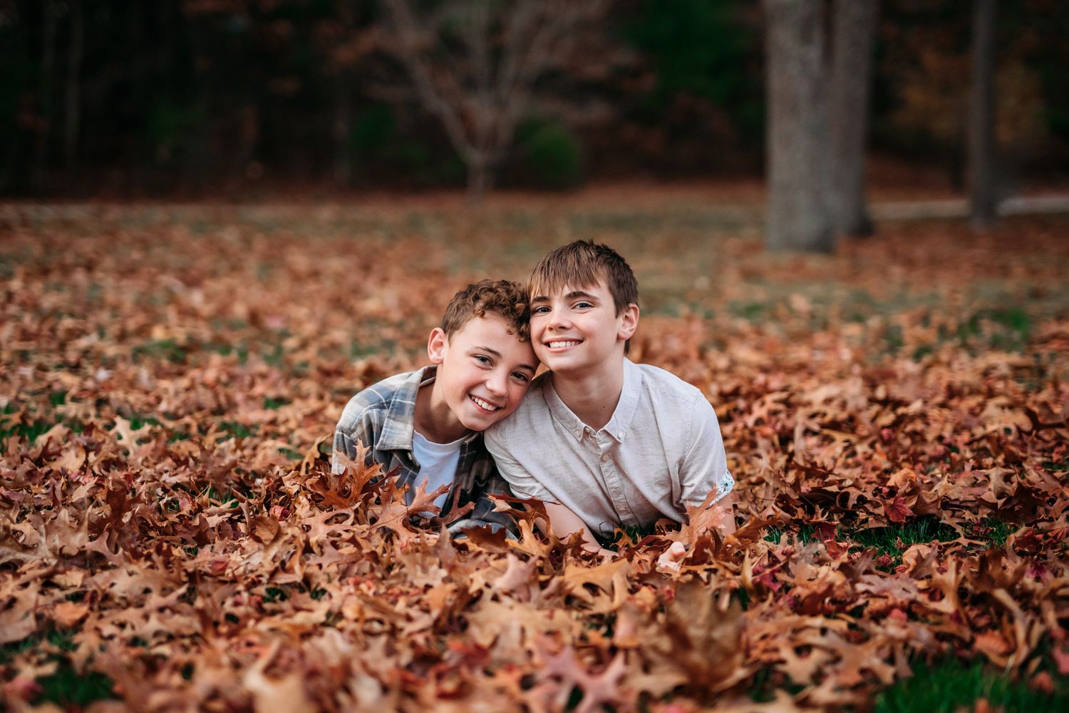 Two young boys lying on colorful autumn leaves playing and laughing together outside.