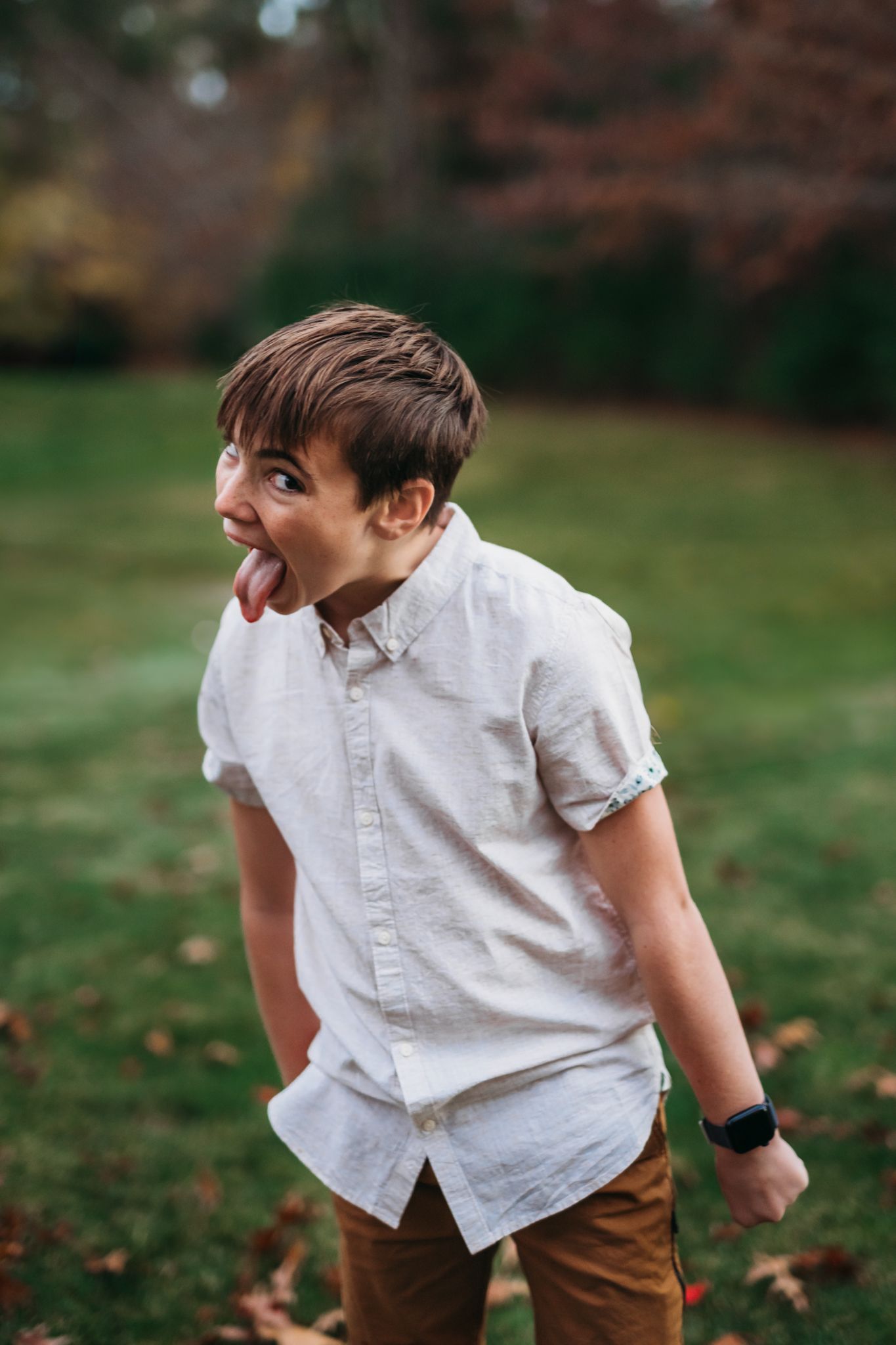 Playful boy in white shirt making silly face and sticking out tongue outdoors in fall.