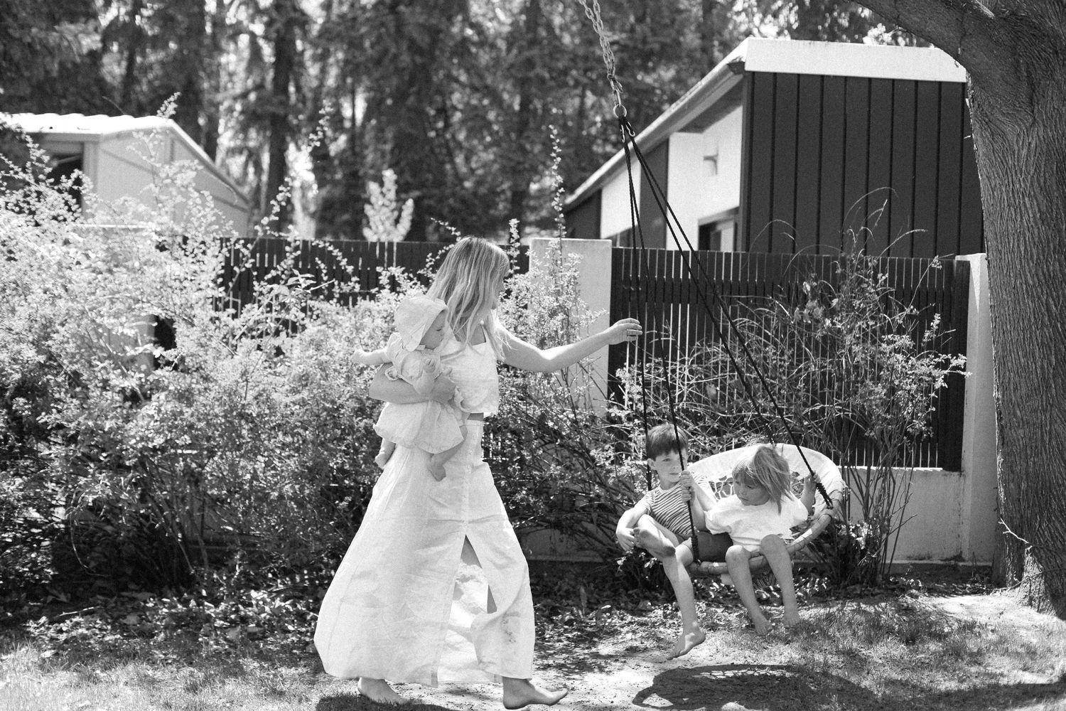 Black and white photo of a mama with baby in flowing dress playing in garden.