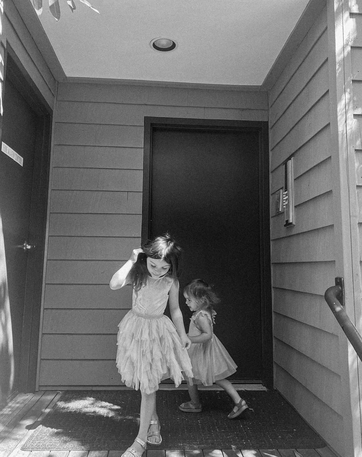 Two children in tulle dresses dance together in a hallway, captured in black and white.