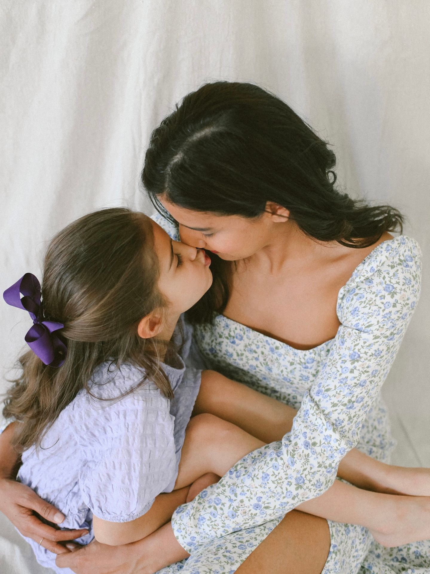 An intimate moment between mama and child wearing floral and white outfits against a white backdrop.