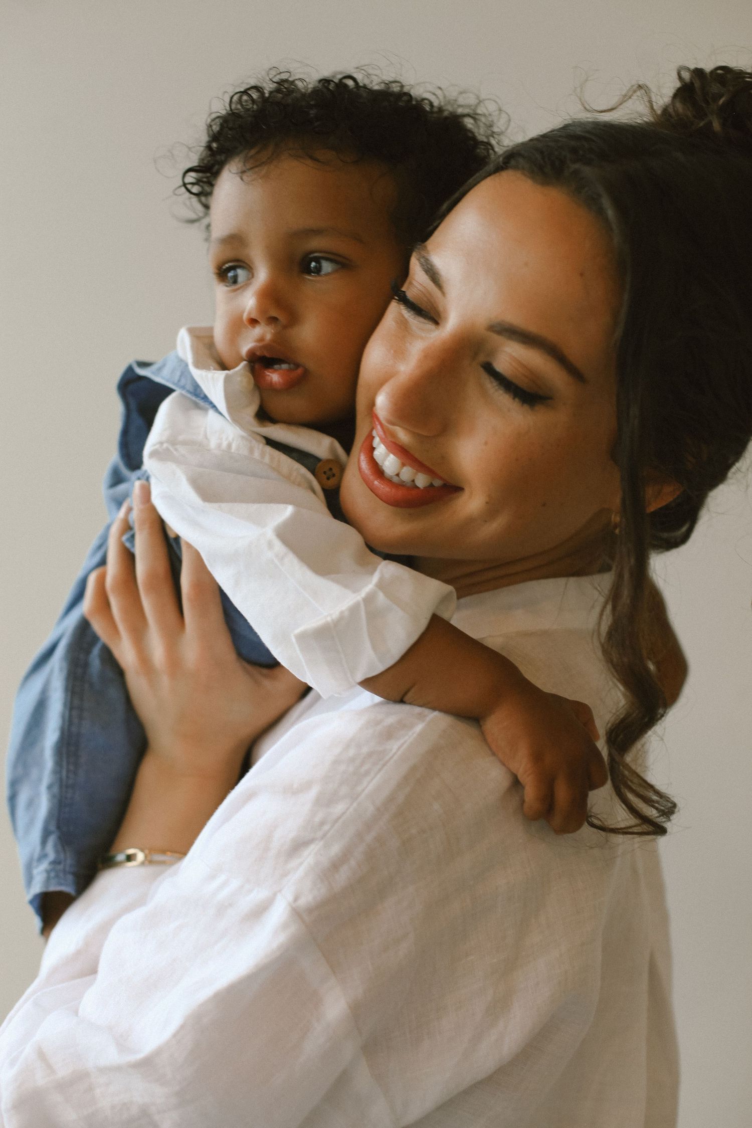 Mother and child share tender moment in intimate portrait against neutral background.