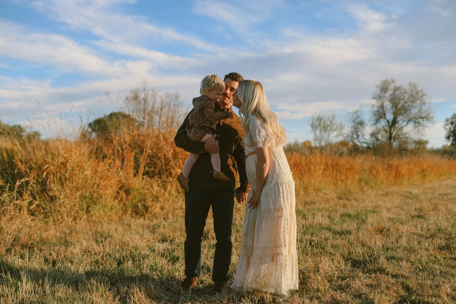 A family shares an intimate moment together in a golden autumn field at sunset.