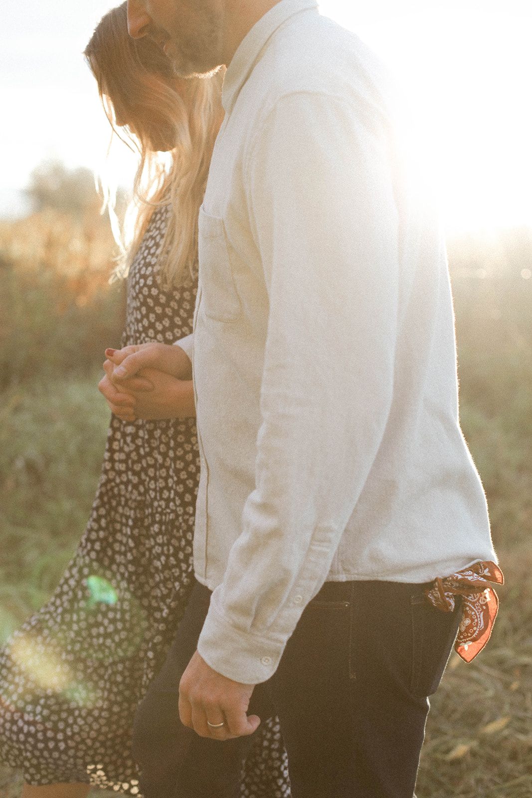 Couple in white and polka dot dress standing in sunlit field.