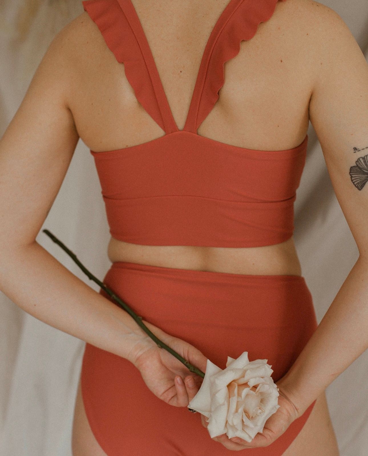 Women wearing a coral two-piece outfit holds a white rose against a light background.