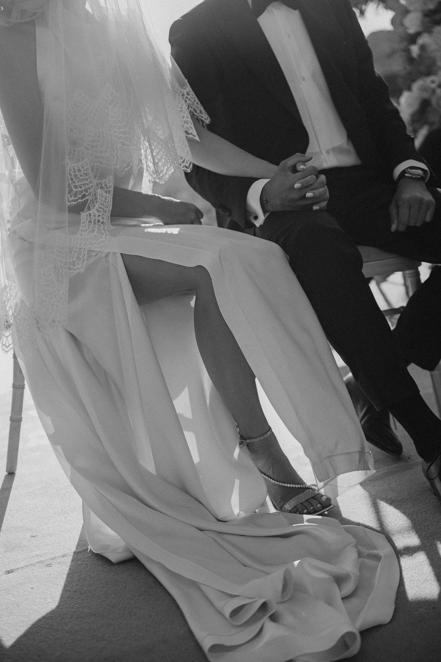 Black and white photograph showing a bride in flowing white dress and groom in dark suit during an intimate wedding ceremony moment.