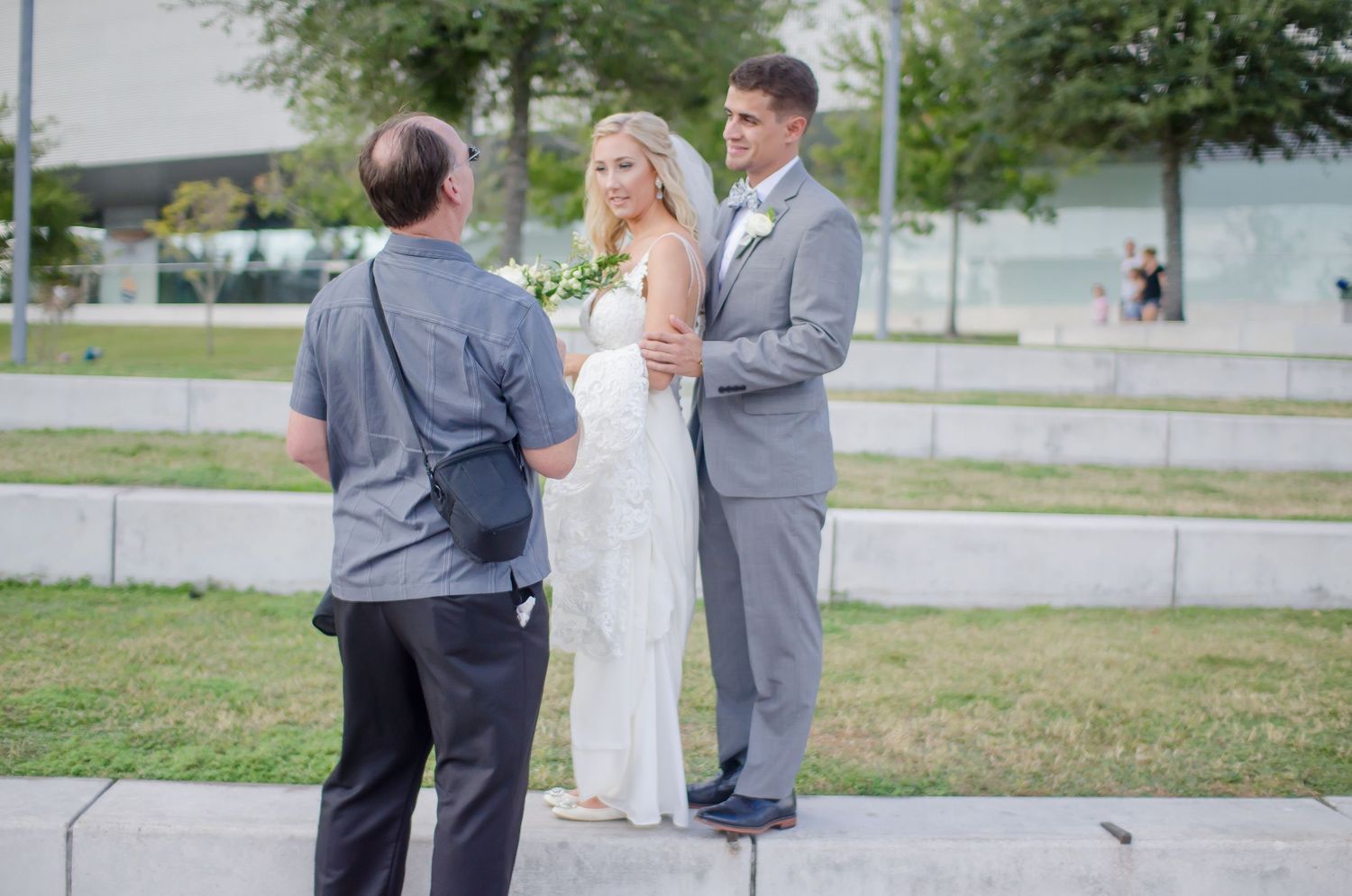 An outdoor wedding ceremony taking place in a park with stone steps and green grass on a bright sunny day.